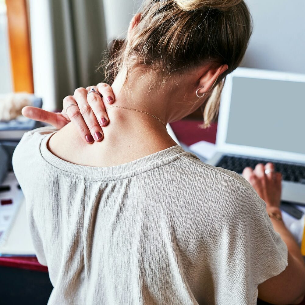 Individual experiencing neck discomfort while working at a computer during an ergonomic and functional assessment